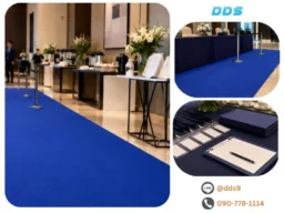 มุมมองนำสายตาผ่านทางเดินพรมลูกฟูกสีน้ำเงินไปยังจุดลงทะเบียนงานประชุมและบาร์น้ำ