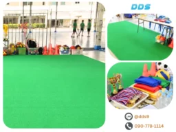 พรมลูกฟูกสีเขียวสดปูบริเวณลานกีฬาโรงเรียน พร้อมโต๊ะวางเหรียญรางวัลและอุปกรณ์สันทนาการกลางแจ้ง